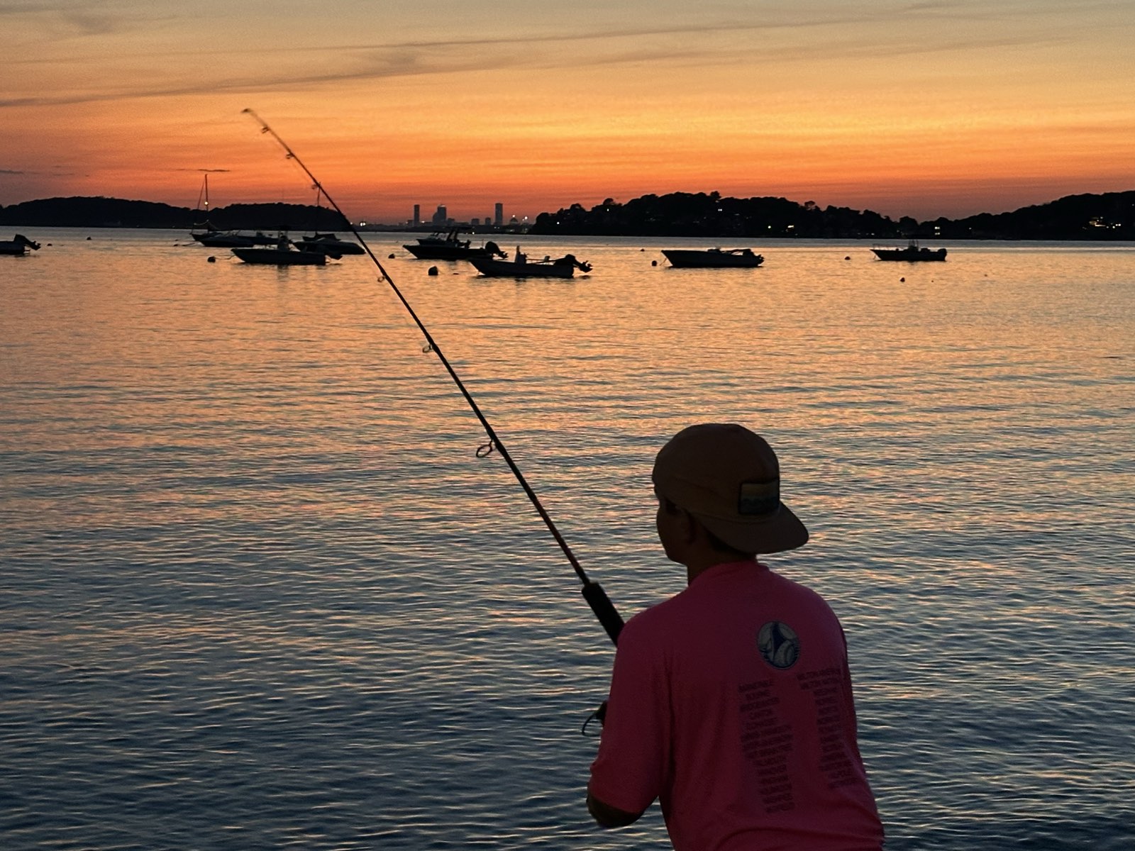 A young angler casting from shore at sunset on the South Shore, MA